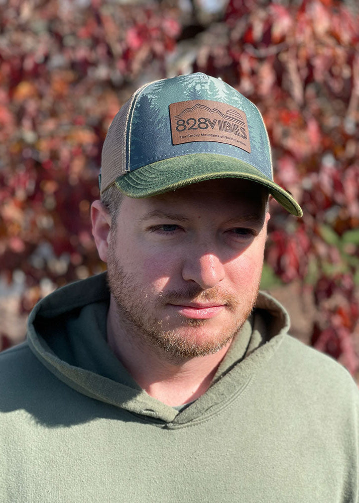 Man wearing a cap with '828 Vibes' logo in front of a blurred natural background