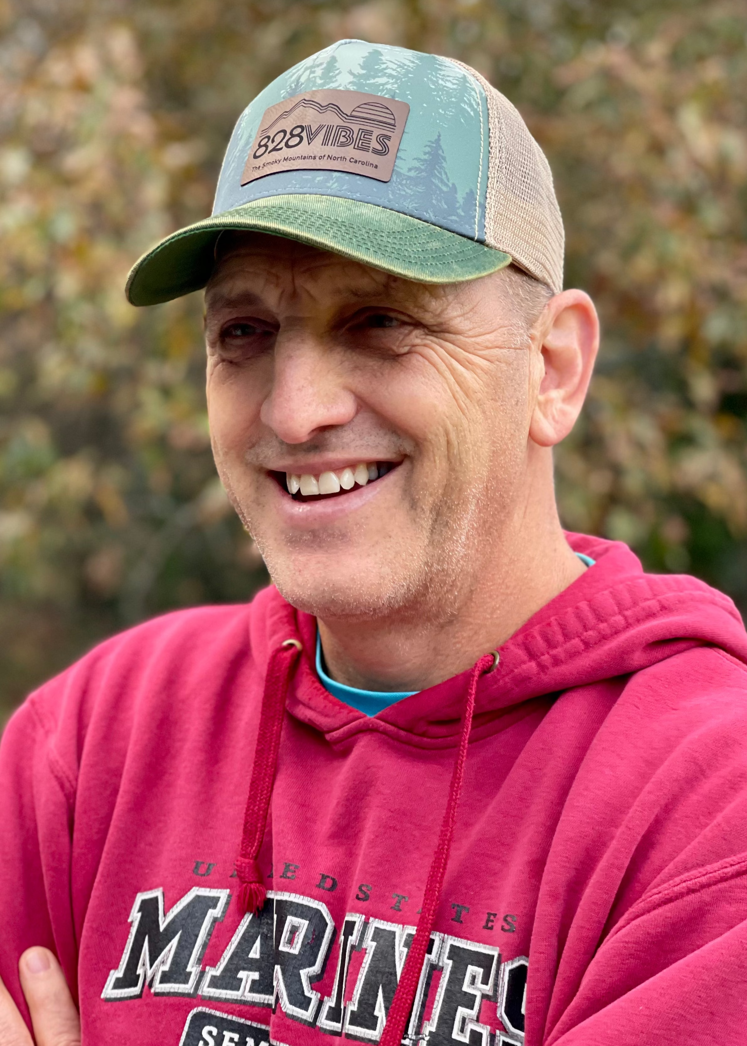 Man wearing a red hoodie with 'Marines' text and a cap outdoors