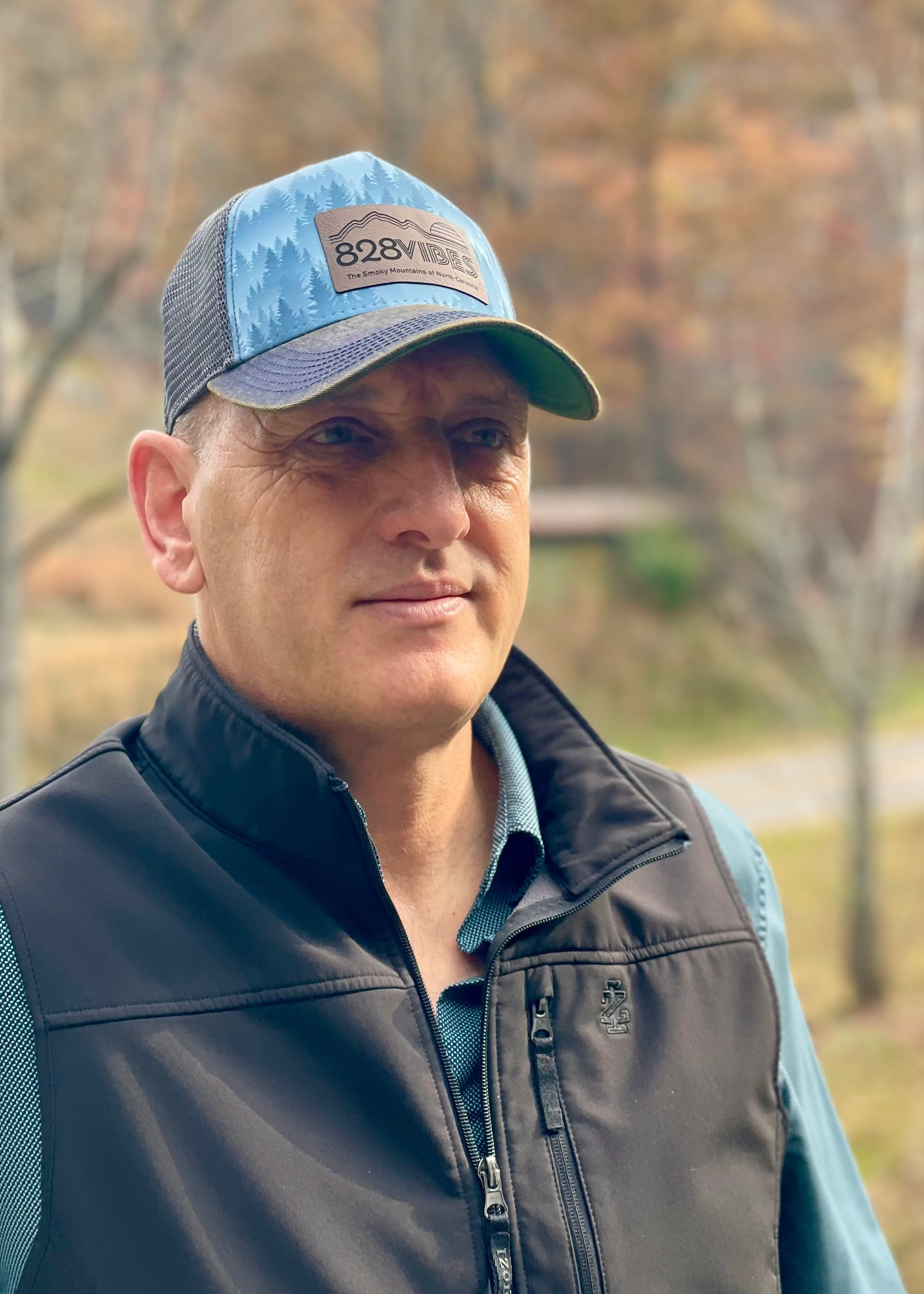 Man wearing a cap and jacket outdoors with trees in the background