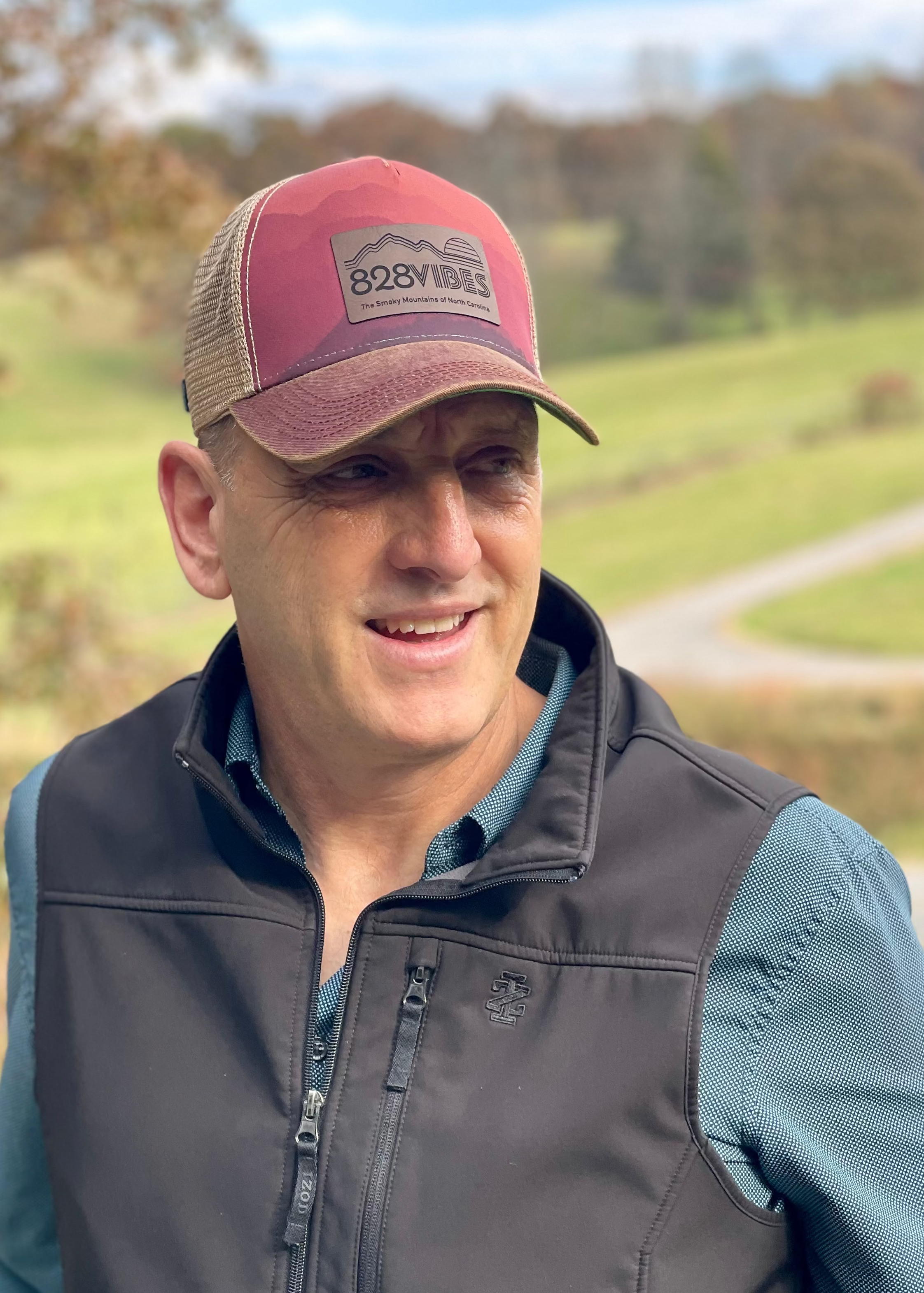 Man wearing a red cap and dark vest outdoors with greenery in the background