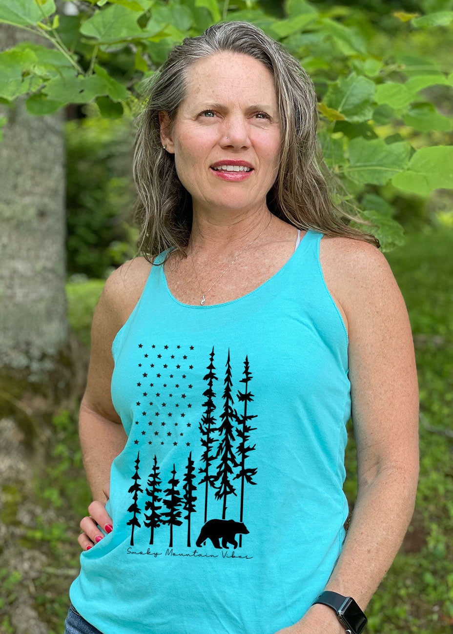 A woman wearing a blue racerback tank top with a black bear and American flag-shaped forest design.