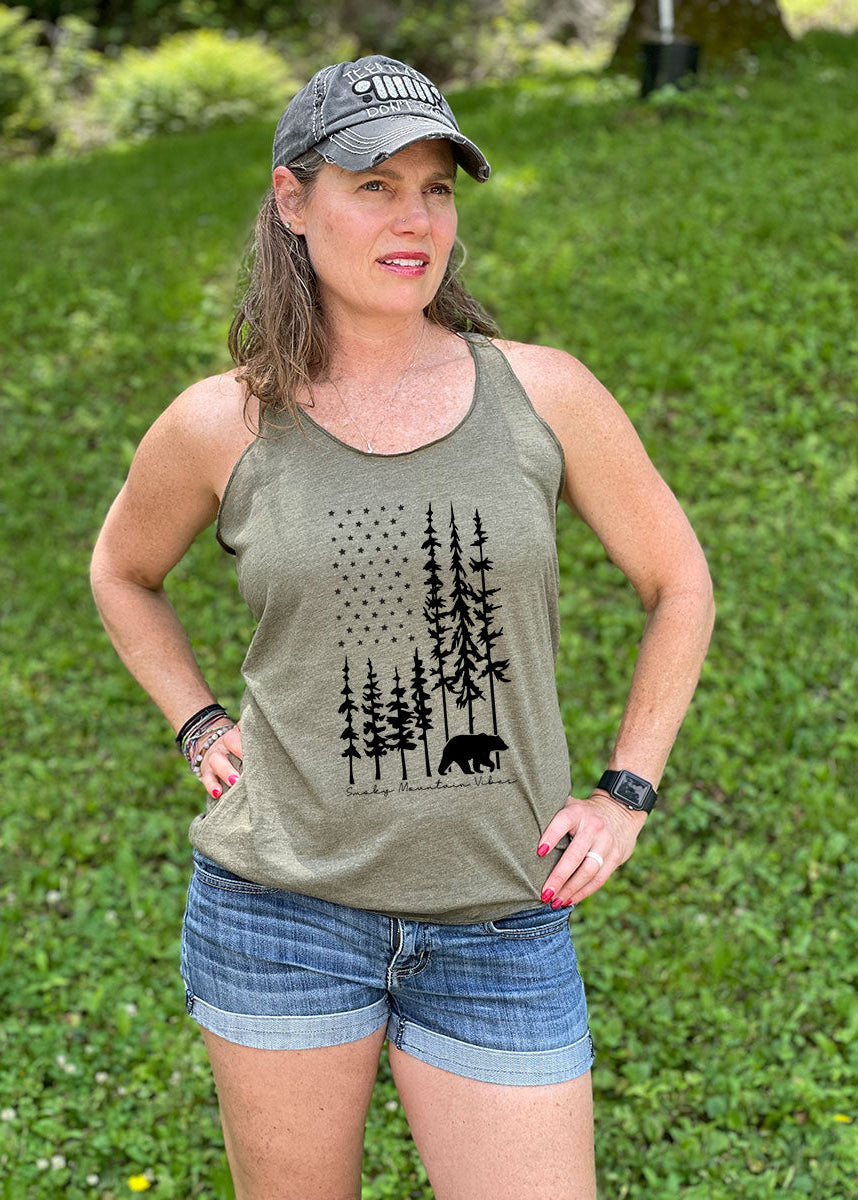 A woman wearing a military green racerback tank top with a black bear and American flag-shaped forest design.