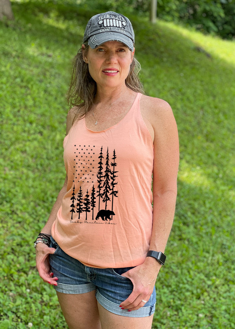 A woman wearing a vintage orange racerback tank top with a black bear and American flag-shaped forest design.