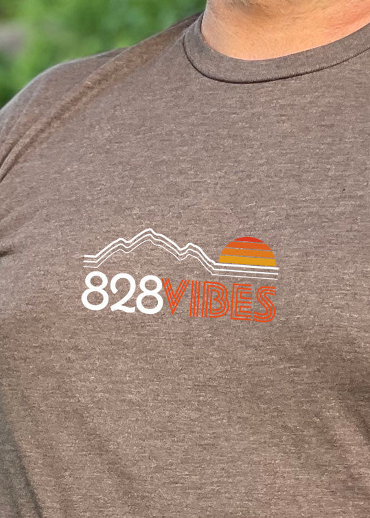 A person standing next to a bicycle, wearing a brown short-sleeve t-shirt with the '828Vibes' logo on it.