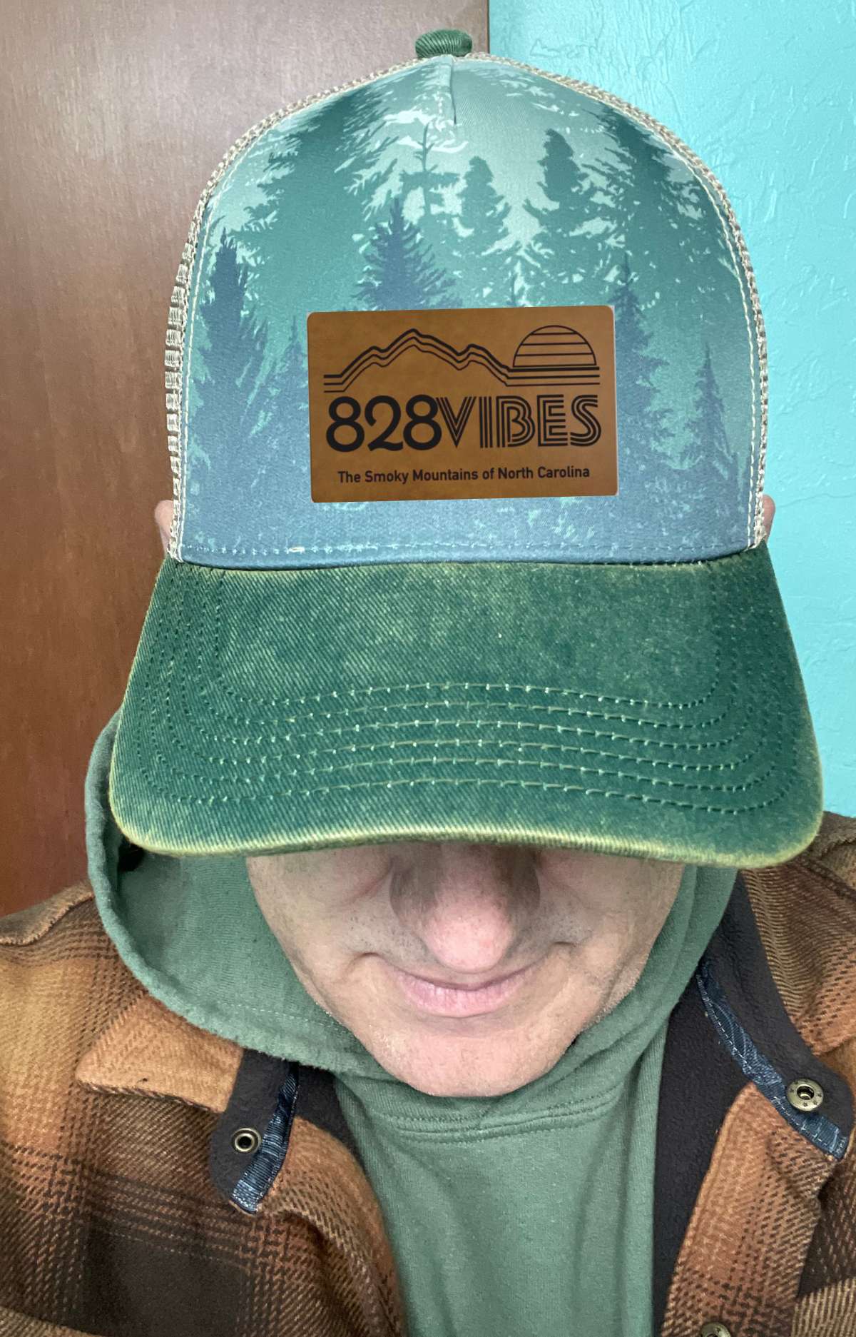 Person wearing a green and blue cap with '828 Vibes' logo, hood up.