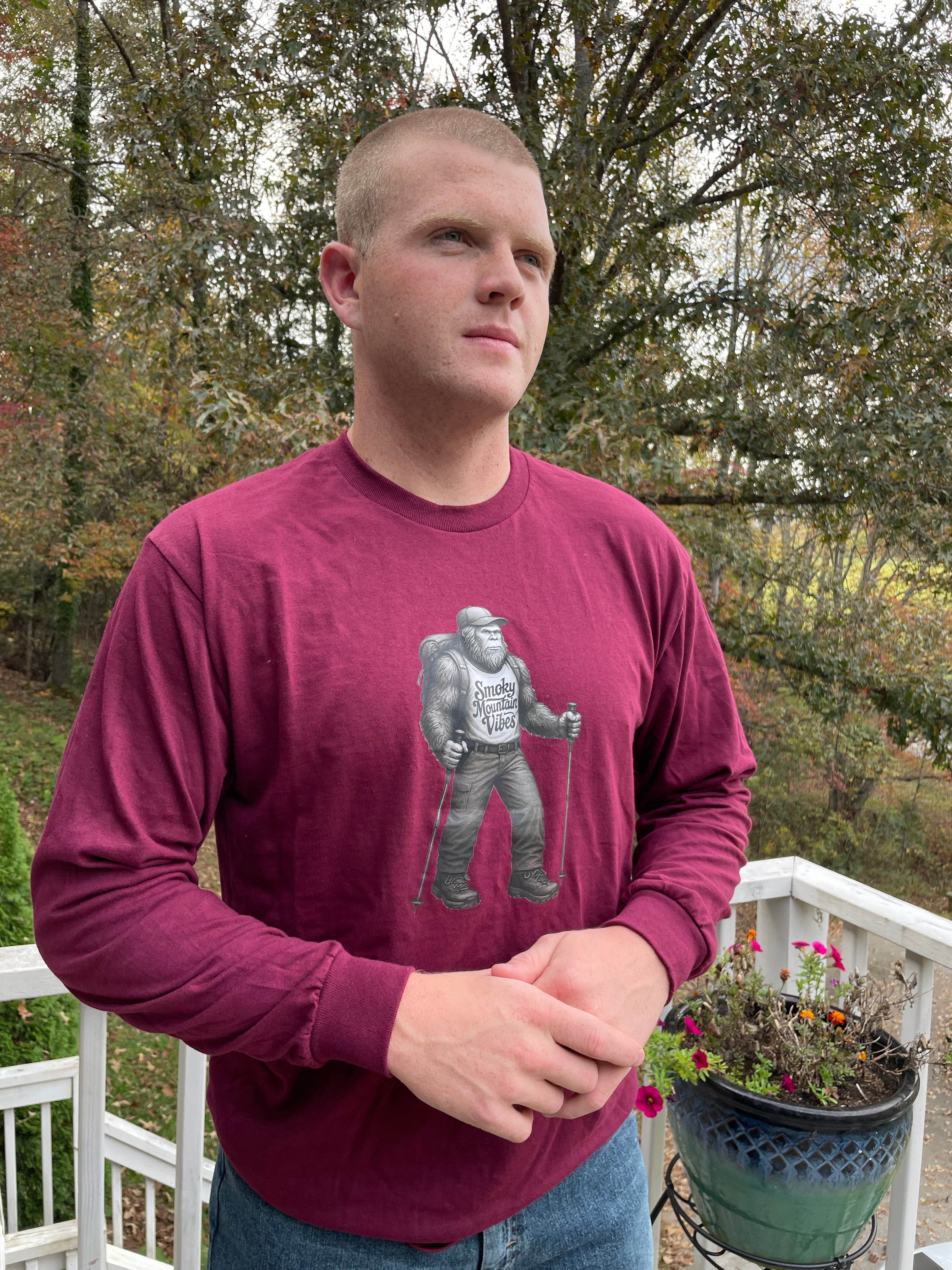 Person wearing a maroon long-sleeve shirt with a hiking bigfoot outdoors