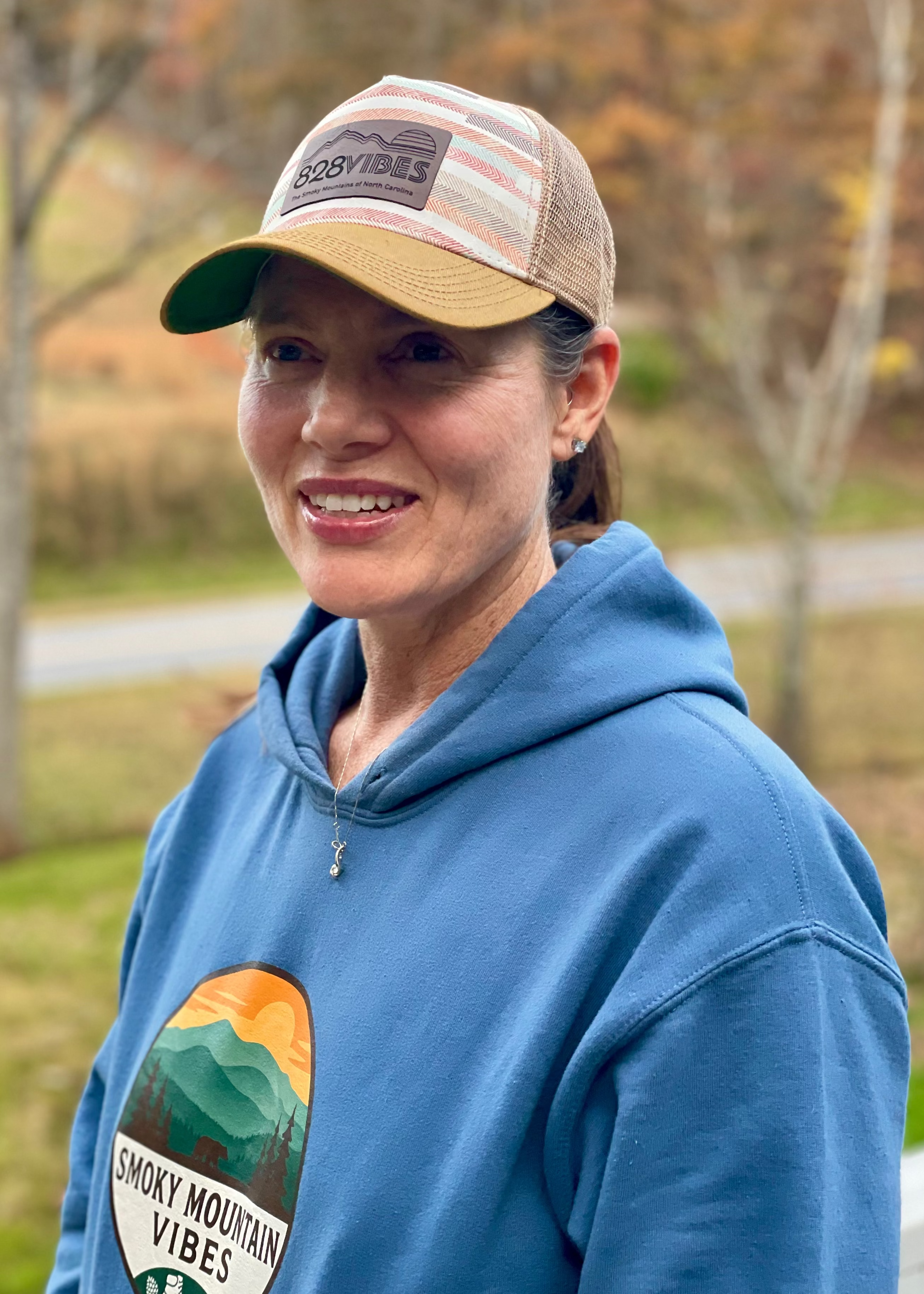 Person wearing a blue hoodie with 'Smoky Mountain Vibes' logo and a cap outdoors.