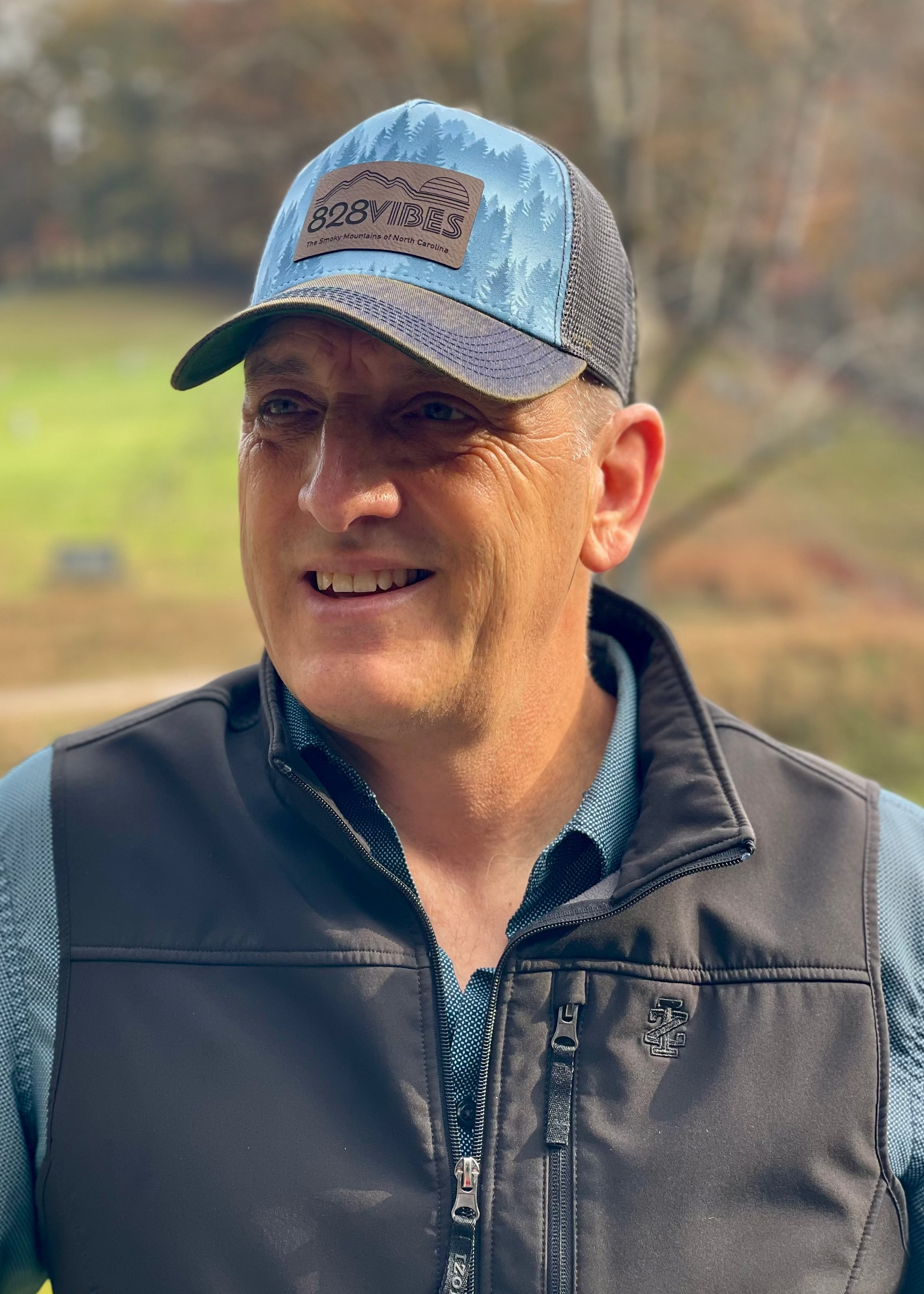 Man wearing a cap and jacket outdoors with a scenic background