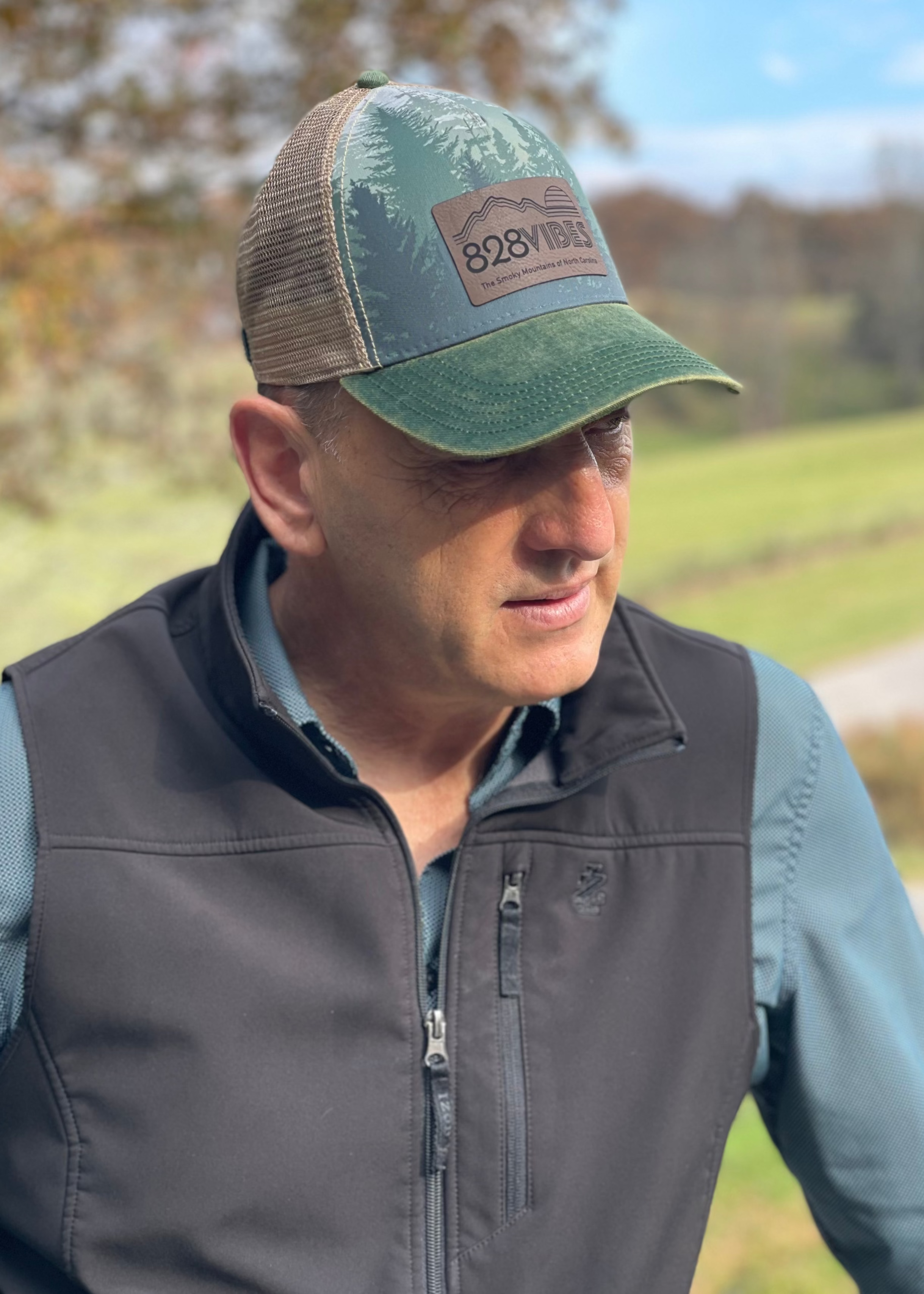 Man wearing a cap with a logo and outdoor clothing in a natural setting