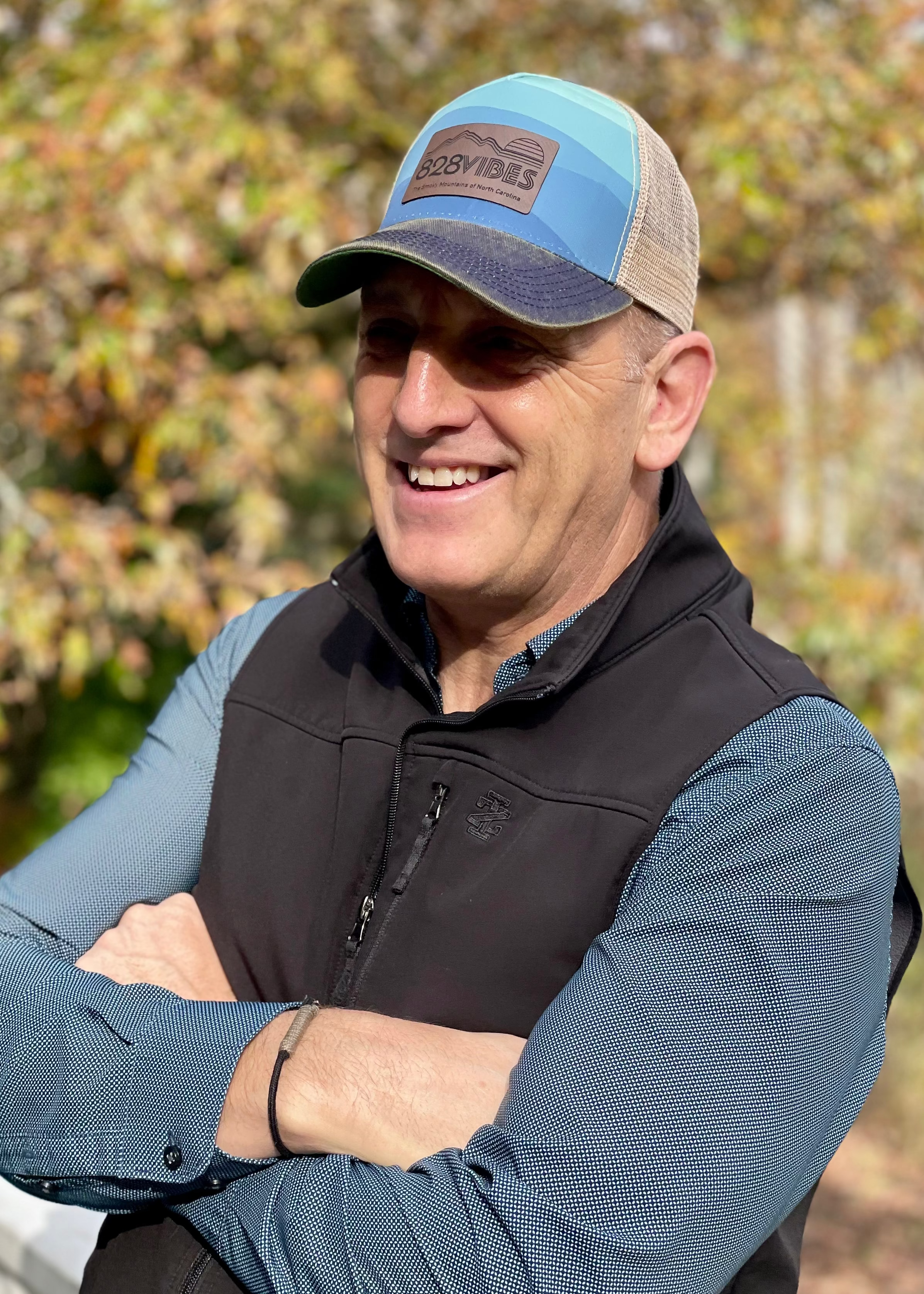 Man wearing a cap and jacket standing in an outdoor setting with trees in the background