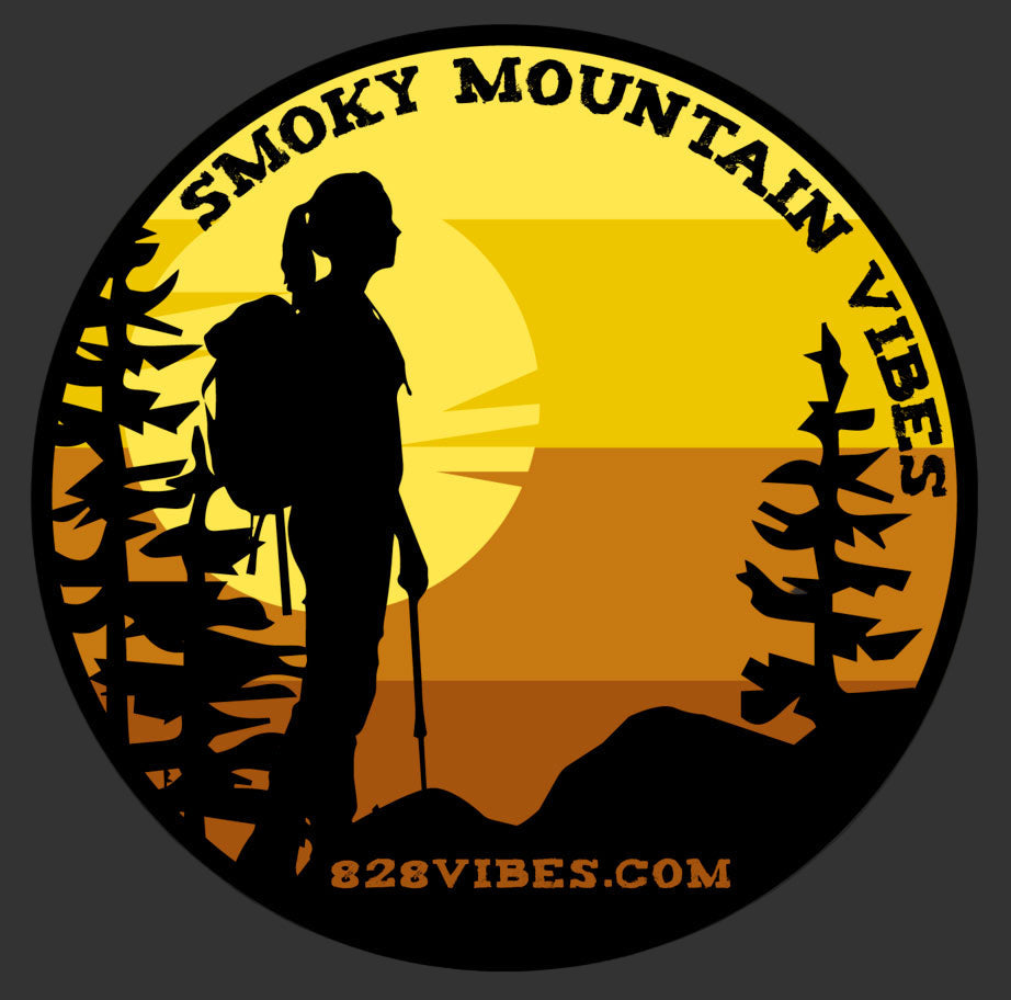 A circular sticker with an illustration of a woman hiking in front of a Smoky Mountain sunset. Text on the sticker reads 'SMOKY MOUNTAIN VIBES' and there's a website address '828VIBES.