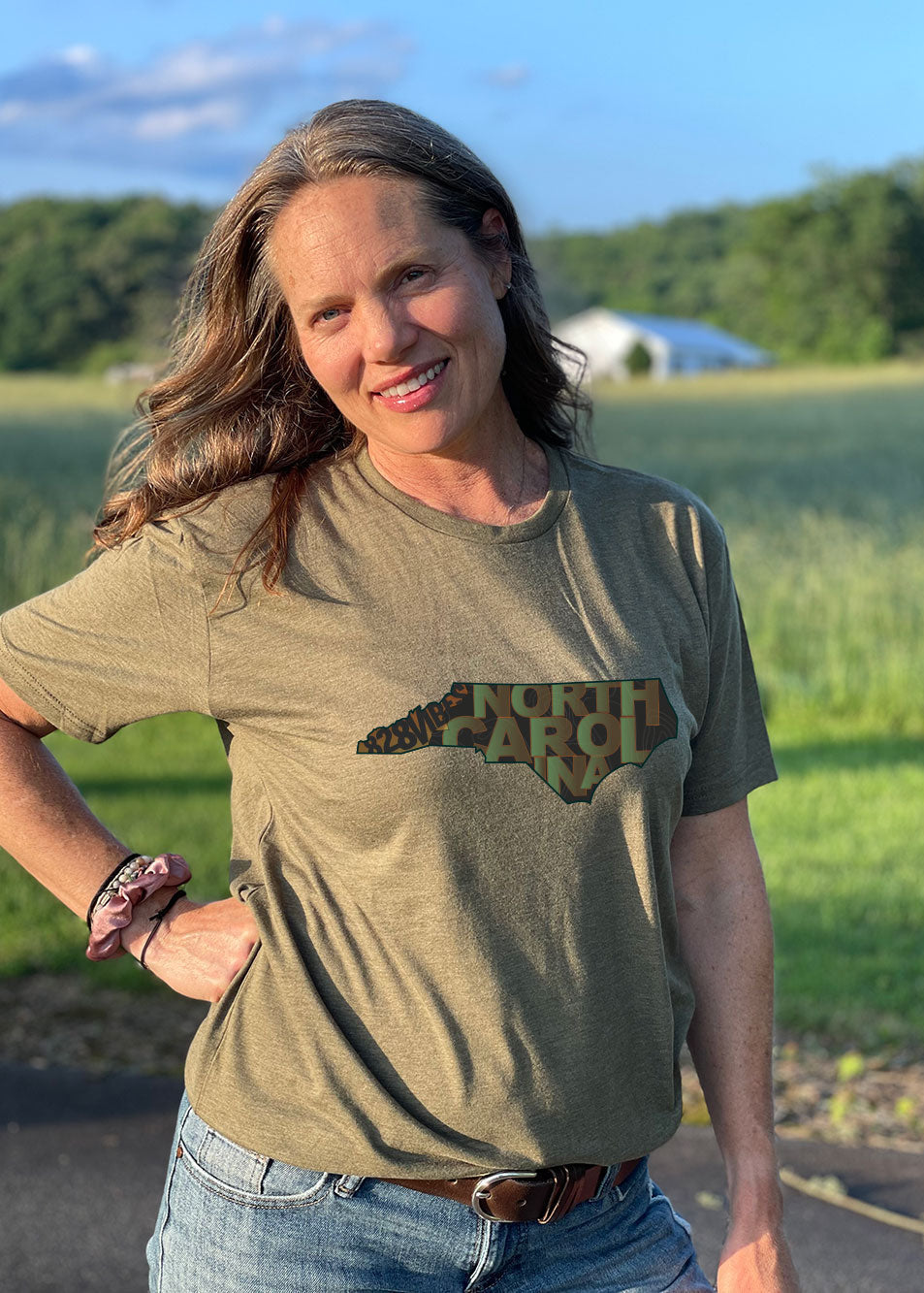 A woman wearing a heather military green short sleeve tee with a north carolina and tactical design.
