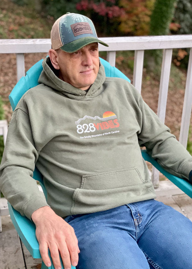 Man sitting on a blue chair wearing a green hoodie with '828' logo and a cap.
