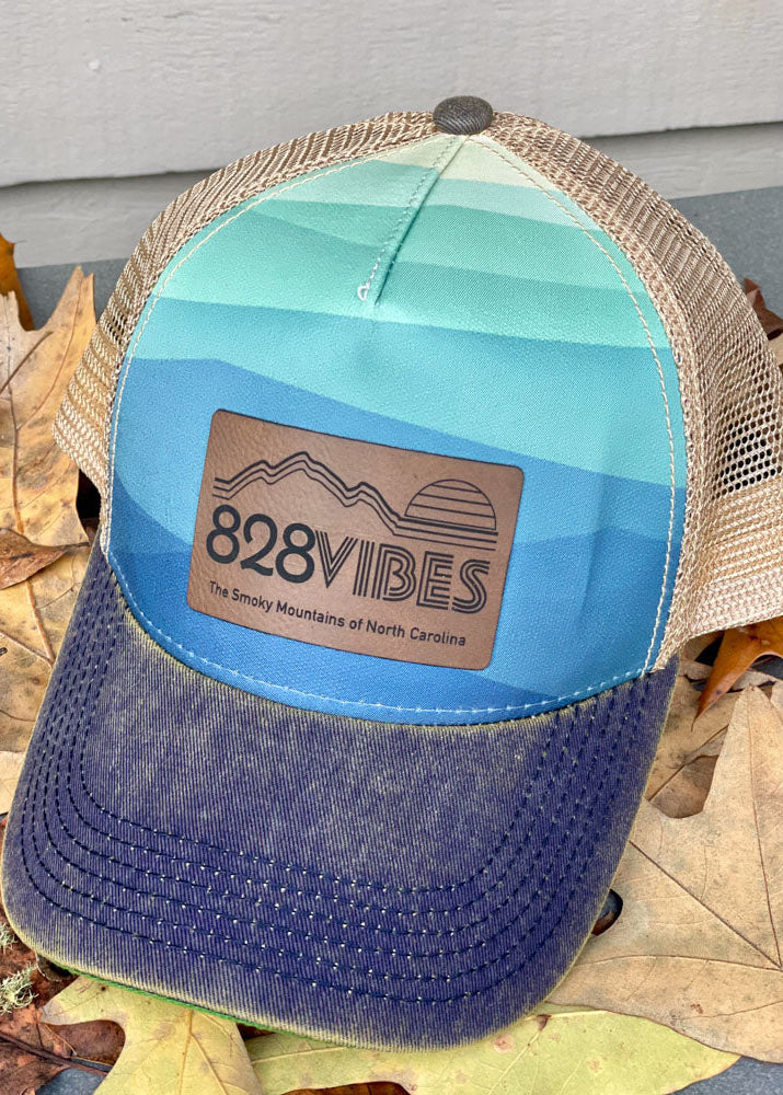 Blue and brown cap with '828 VIBES' logo on a leafy background