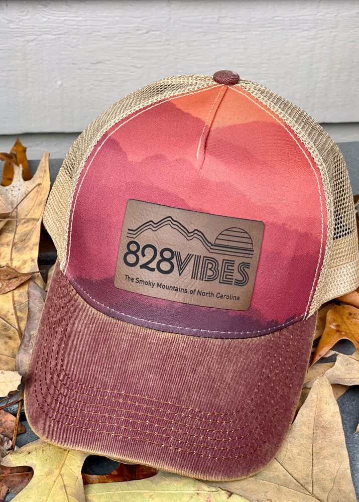Pink and beige trucker hat with '828 Vibes' logo on a background of fallen leaves.